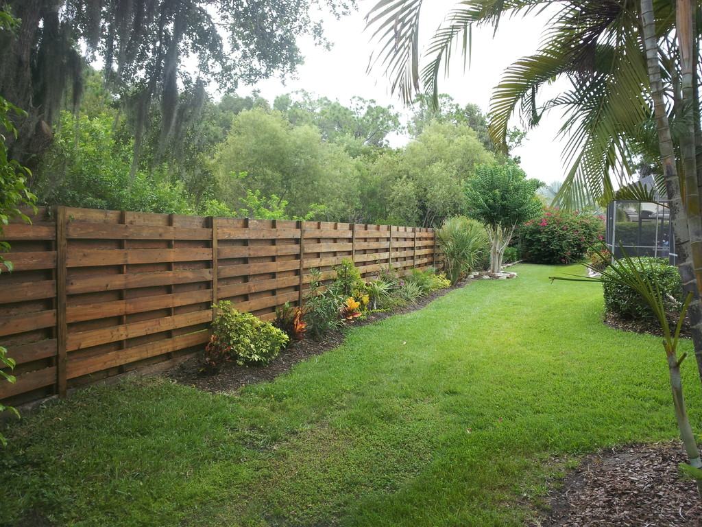 A long horizontal wood privacy fence along a green backyard lawn after cleaning, restored to an even brown.